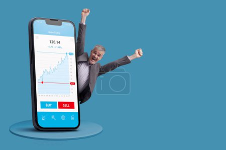 Successful cheerful businessman making money in online trading: financial app on big smartphone, blank copy space