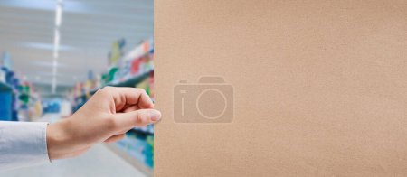 Photo for Hand holding a recycled paper sign and supermarket aisle in the background, grocery shopping and commerce concept - Royalty Free Image