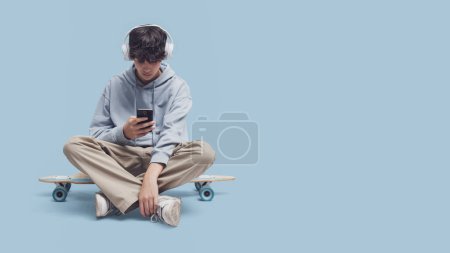 Foto de Patinador con auriculares y sentado en su patín, que se conecta con su teléfono inteligente y escuchar música, espacio de copia en blanco - Imagen libre de derechos