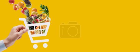 Foto de Mano sosteniendo un icono de carro lleno de comestibles frescos: compras en línea y aplicación de entrega - Imagen libre de derechos