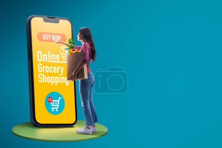 Photo for Woman holding a grocery bag and doing online grocery shopping, she is ordering products on the mobile app - Royalty Free Image