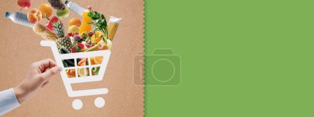 Téléchargez les photos : Main tenant une icône de panier plein d'épicerie fraîche : application d'épicerie et de livraison en ligne - en image libre de droit