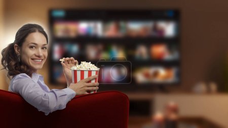Young woman smiling at camera and watching movies on her smart TV at home, entertainment and cinema concept