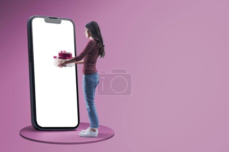 Photo for Happy woman doing online shopping on a big smartphone and receiving gifts, blank screen on the smartphone, copy spce - Royalty Free Image