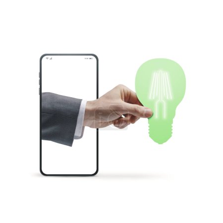 Photo for Businessman's hand coming out of a smartphone screen and holding a LED lamp, energy efficiency and sustainability concept, isolated on white background - Royalty Free Image