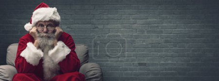 Téléchargez les photos : Père Noël assis sur le fauteuil et attendant Noël, il repose sa tête sur ses mains - en image libre de droit