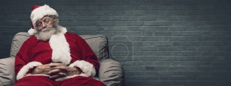Téléchargez les photos : Somnolent Père Noël faire une sieste et se détendre sur le fauteuil la veille de Noël - en image libre de droit