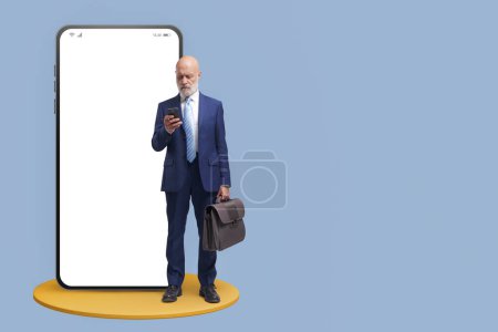 Téléchargez les photos : Homme d'affaires d'entreprise debout à côté d'un grand smartphone avec écran blanc, il vérifie son téléphone portable - en image libre de droit
