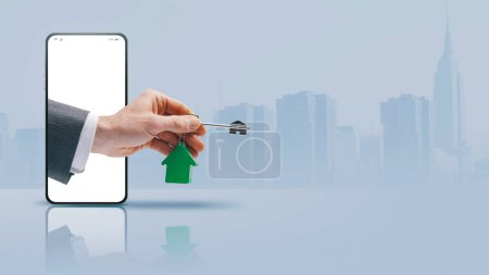 Photo for Real estate agent hand in a smartphone screen holding your new house keys, real estate app concept, copy space - Royalty Free Image