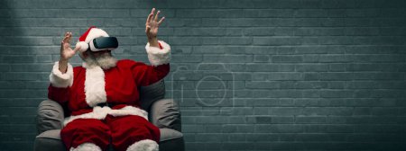 Photo for Santa Claus experiencing virtual reality, he is wearing VR glasses and interacting with a virtual environment - Royalty Free Image
