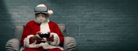 Photo for Santa Claus experiencing virtual reality at home and playing videogames using a controller, he is wearing a VR headset - Royalty Free Image