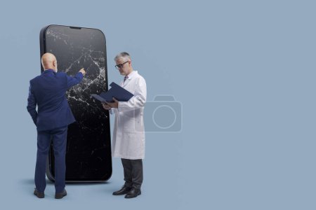 Photo for Smartphone and electronics repair service concept: big mobile phone with broken screen, customer and technician doctor holding a clipboard, blank copy space - Royalty Free Image