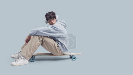 Foto de Adolescente fresco posando con un monopatín, aislado sobre fondo gris - Imagen libre de derechos