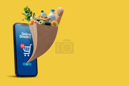 Photo for Online grocery app on smartphone and full grocery bag coming out of the smartphone screen, copy space - Royalty Free Image