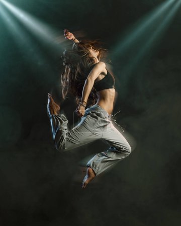 Téléchargez les photos : Professional female dancer performing on stage, she is jumping surrounded by smoke, dance and entertainment concept - en image libre de droit