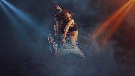 Photo for Professional female dancer performing on stage, she is jumping surrounded by smoke, dance and entertainment concept - Royalty Free Image