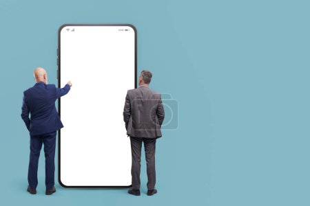 Téléchargez les photos : Business people standing in front of a big smartphone with blank screen, they are using mobile apps - en image libre de droit