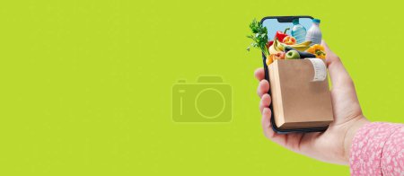 Téléchargez les photos : Femme tenant son smartphone et faisant des courses en ligne, elle reçoit des aliments frais et des boissons - en image libre de droit