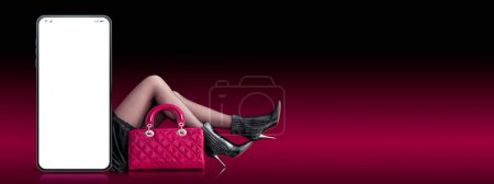Photo for Smartphone with blank screen and fashionable woman with bag and high-heeled shoes, online shopping concept, copy space - Royalty Free Image