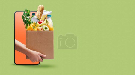 Téléchargez les photos : Mains tenant une boîte pleine d'épicerie fraîche et d'applications d'épicerie en ligne sur smartphone - en image libre de droit