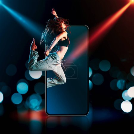 Téléchargez les photos : Professional dancer jumping out of a smartphone screen and stage lights in the background: entertainment and apps concept - en image libre de droit