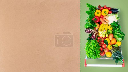 Supermarket shopping cart full of fresh vegetables and fruits, copy space