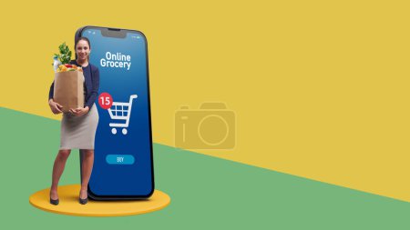 Foto de Mujer feliz sosteniendo una bolsa de supermercado completa y un teléfono inteligente: concepto de aplicación de compras en línea - Imagen libre de derechos