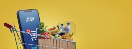 Téléchargez les photos : Supermarket shopping cart full of groceries and smartphone with online grocery shopping app, copy space - en image libre de droit