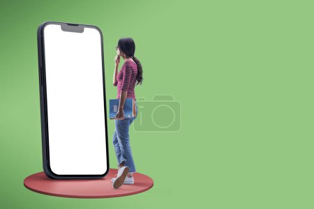 Photo for Female student holding notebooks and using a big smartphone with blank screen, e-learning concept, copy space - Royalty Free Image