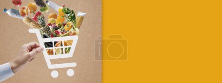 Foto de Mano sosteniendo un icono de carrito de la compra lleno de comestibles frescos: compras en línea y aplicación de entrega - Imagen libre de derechos
