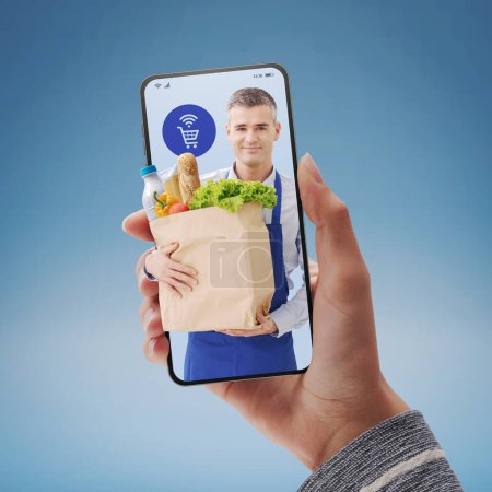 Téléchargez les photos : Application d'épicerie en ligne : assistant de magasin tenant un sac d'épicerie complet dans un écran de smartphone - en image libre de droit