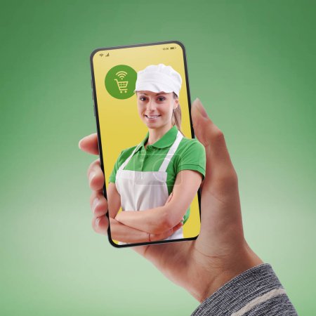 Foto de Customer holding a smartphone and shop assistant: online grocery shopping app concept - Imagen libre de derechos