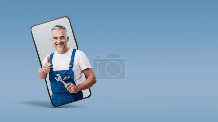 Téléchargez les photos : Réparateur et plombier joyeux donnant un pouce vers le haut dans un vidéocall smartphone et souriant, concept de service en ligne - en image libre de droit