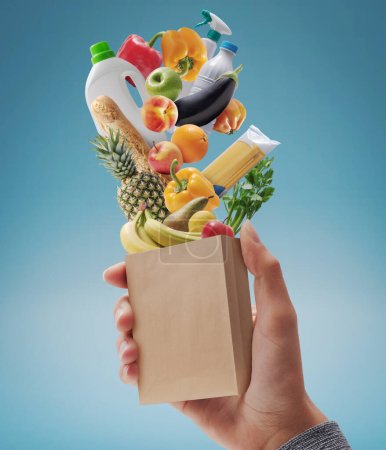 Téléchargez les photos : Customer holding a miniature paper bag with fresh groceries falling inside, grocery shopping concept - en image libre de droit