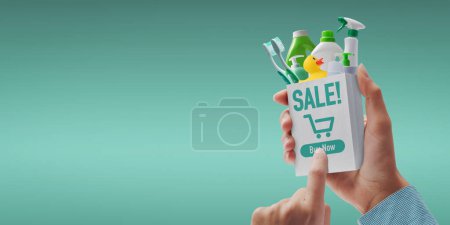 Photo for Customer holding a miniature shopping bag and ordering detergents online, she is pressing the buy now button - Royalty Free Image