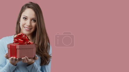 Téléchargez les photos : Joyeux belle jeune femme tenant une boîte cadeau avec ruban rouge - en image libre de droit