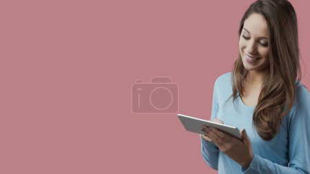 Téléchargez les photos : Jeune femme souriante utilisant une tablette numérique sur fond rouge - en image libre de droit