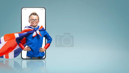 Foto de Sonriendo divertido super héroe chico posando con los brazos akimbo en un videocall smartphone y sonriendo - Imagen libre de derechos