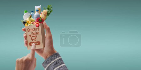 Téléchargez les photos : Client tenant un sac miniature et commandant une épicerie en ligne, elle appuie sur le bouton acheter maintenant - en image libre de droit