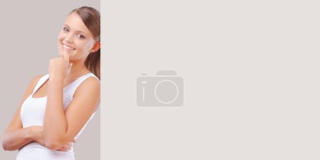 Photo for Smiling young woman peeking from behind a big blank sign, communication concept - Royalty Free Image