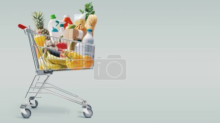Foto de Carro de compras lleno de alimentos frescos y productos para el hogar: concepto de compras de comestibles - Imagen libre de derechos