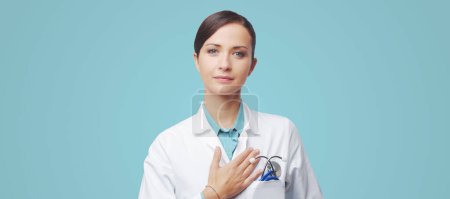 Foto de Atractiva cardióloga con estetoscopio y bata de laboratorio, tocando su pecho
. - Imagen libre de derechos