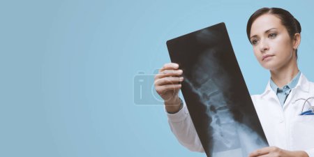 Téléchargez les photos : Radiologiste féminine confiante vérifiant l'image radiographique de la colonne vertébrale
. - en image libre de droit