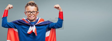 Photo for Cute smiling superhero showing off muscles, he is wearing a Union Jack flag as a cape - Royalty Free Image