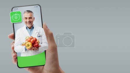 Téléchargez les photos : Nutrition professionnelle tenant des aliments sains et vidéocellulaire, concept de médecin en ligne - en image libre de droit