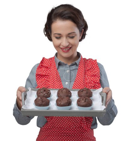 Téléchargez les photos : Femme vintage souriante dans un tablier servant des muffins au chocolat faits maison sur un plateau - en image libre de droit