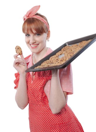 Photo for Happy vintage style housewife tasting her freshly baked homemade sweets, she is holding a baking tray full of cookies - Royalty Free Image