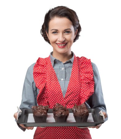Foto de Mujer vintage sonriente sosteniendo una bandeja para hornear con magdalenas hechas en casa de chocolate - Imagen libre de derechos