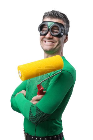 Foto de Divertido superhéroe alegre sosteniendo un rodillo de pintura y sonriendo a la cámara
. - Imagen libre de derechos
