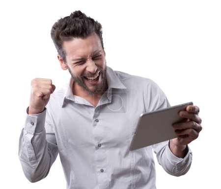 Foto de Alegre hombre sonriente recibiendo buenas noticias en la tableta con el puño levantado - Imagen libre de derechos